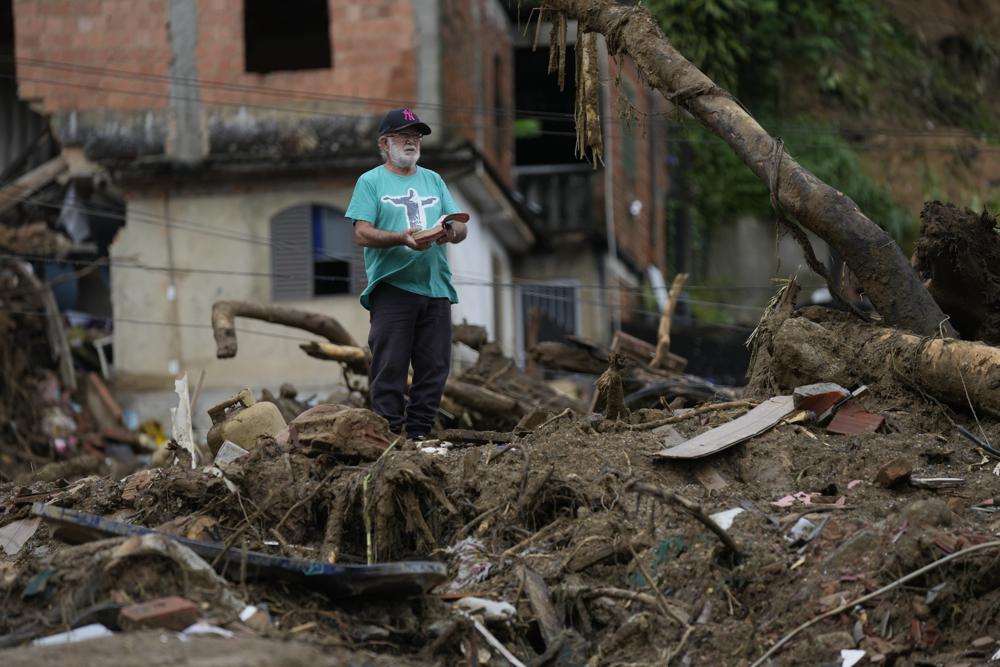 A man with a Bible stands on the debris of homes destroyed by mudslides on the third day of rescue efforts in Petropolis, Brazil, Friday, Feb. 18, 2022. (AP Photo/Silvia Izquierdo)